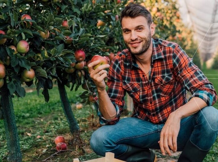 Elma bahçesinde bir çiftçi, sağlıklı ve kırmızı bir elmayı gösteriyor. Bor ve Molibden çözümleri ile giderilmiş mikro besin eksiklikleri sayesinde elde edilmiş kaliteli meyve.