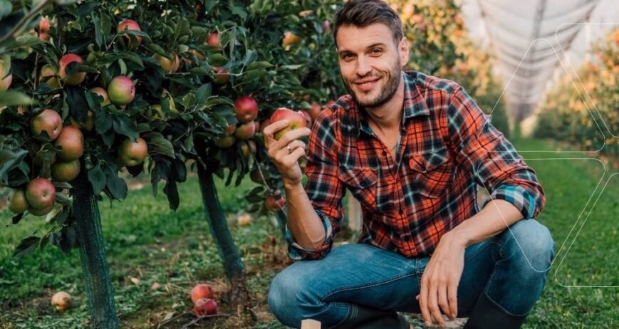 Elma bahçesinde bir çiftçi, sağlıklı ve kırmızı bir elmayı gösteriyor. Bor ve Molibden çözümleri ile giderilmiş mikro besin eksiklikleri sayesinde elde edilmiş kaliteli meyve.