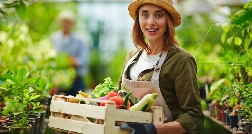 Serada hasat: Şapkalı, önlüklü bir kadın elinde taze sebzelerle dolu kasayı tutuyor. Potasyum gübreleri ile artırılmış meyve kalitesi ve yüksek verim gösteren ürünler.